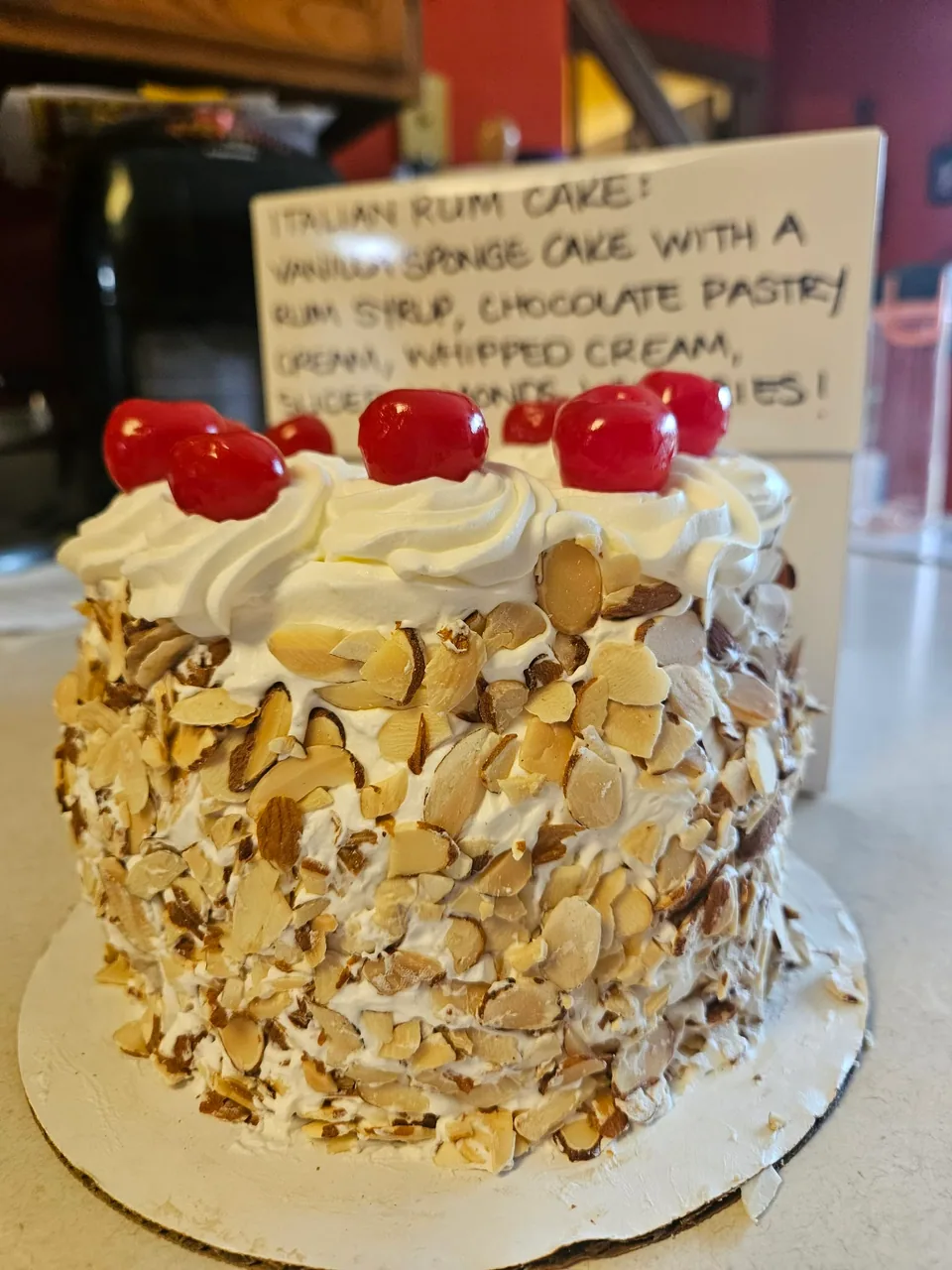 Cream-colored cake with sliced almonds and red cherries on top