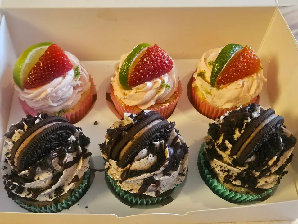 Box of assorted decorated cupcakes with fruit, cookies, and chocolate drizzle