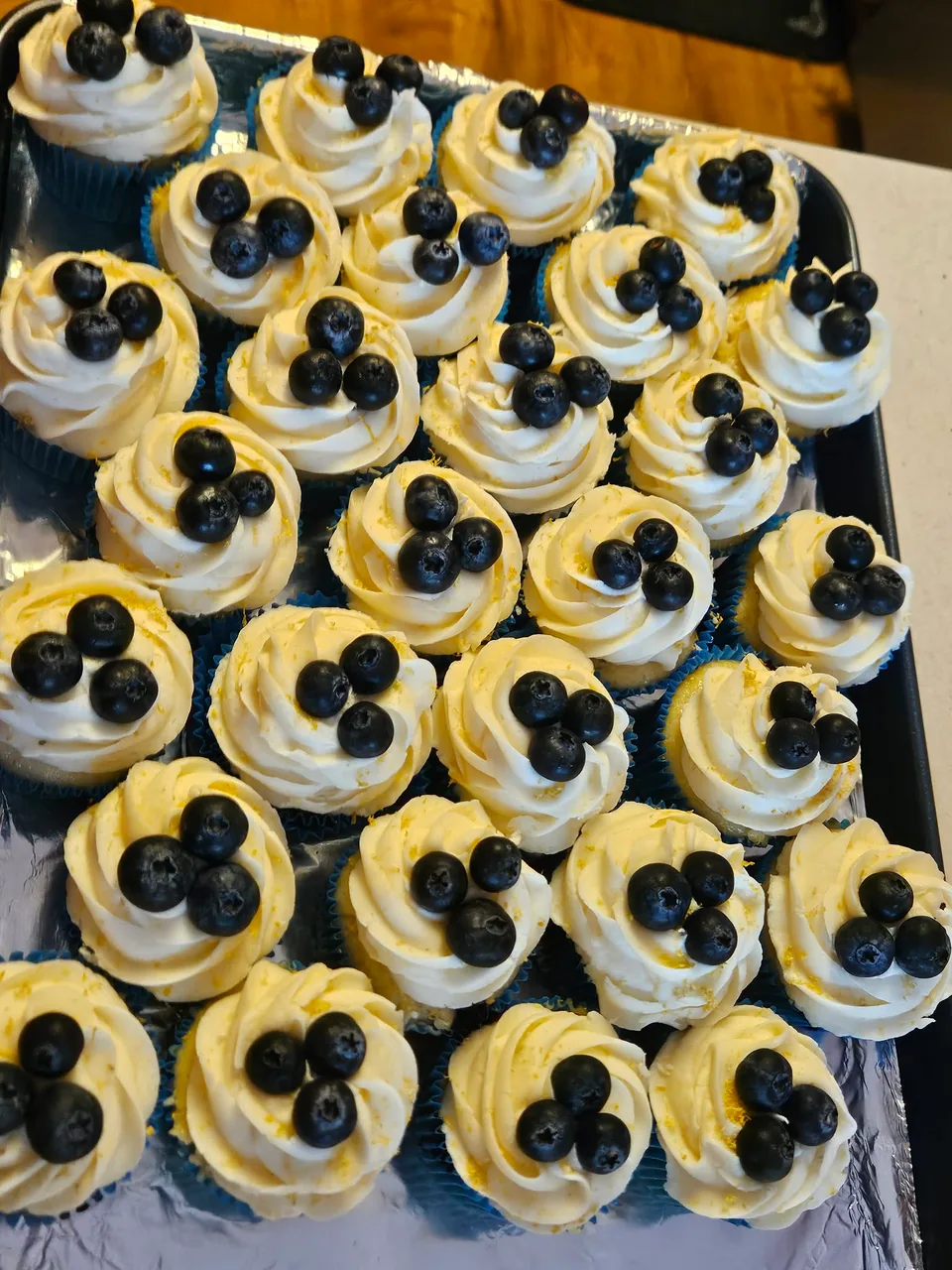 Large tray of cupcakes topped with blueberries and cream frosting