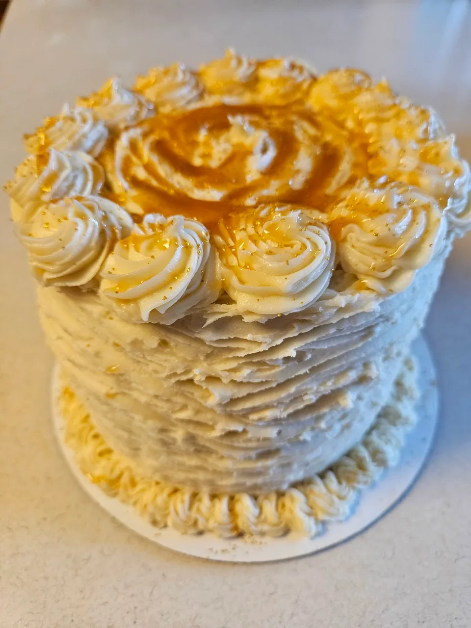 Caramel cake with cream frosting, piped rosettes, and caramel drizzle