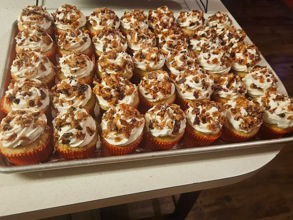 Tray of maple bacon cupcakes with piped frosting and bacon pieces
