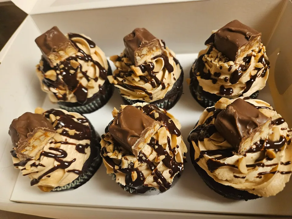 Snickers cupcakes topped with piped frosting, chocolate drizzle, and candy pieces