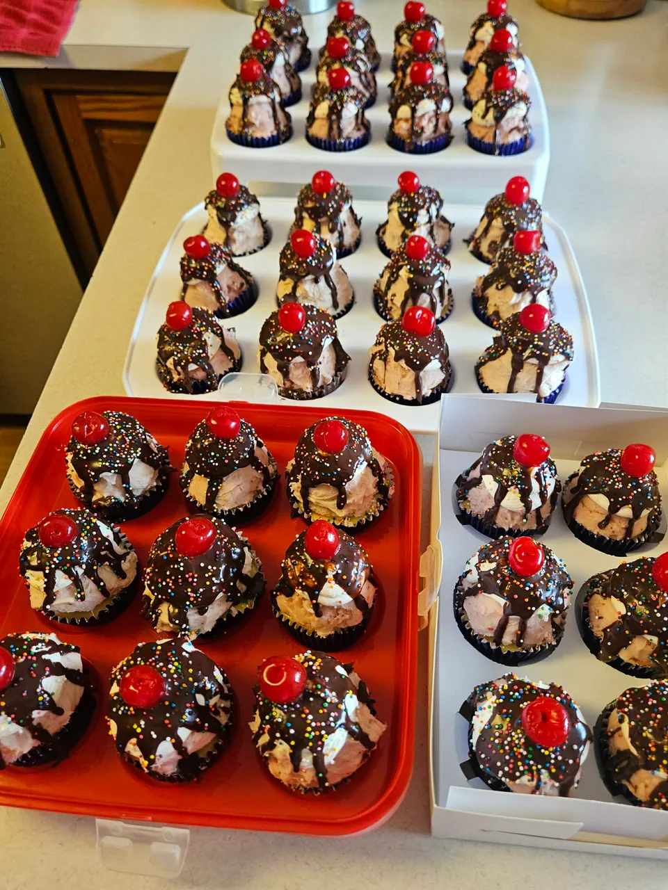Assortment of ice cream sundae cupcakes with cherries, chocolate drizzle, and sprinkles