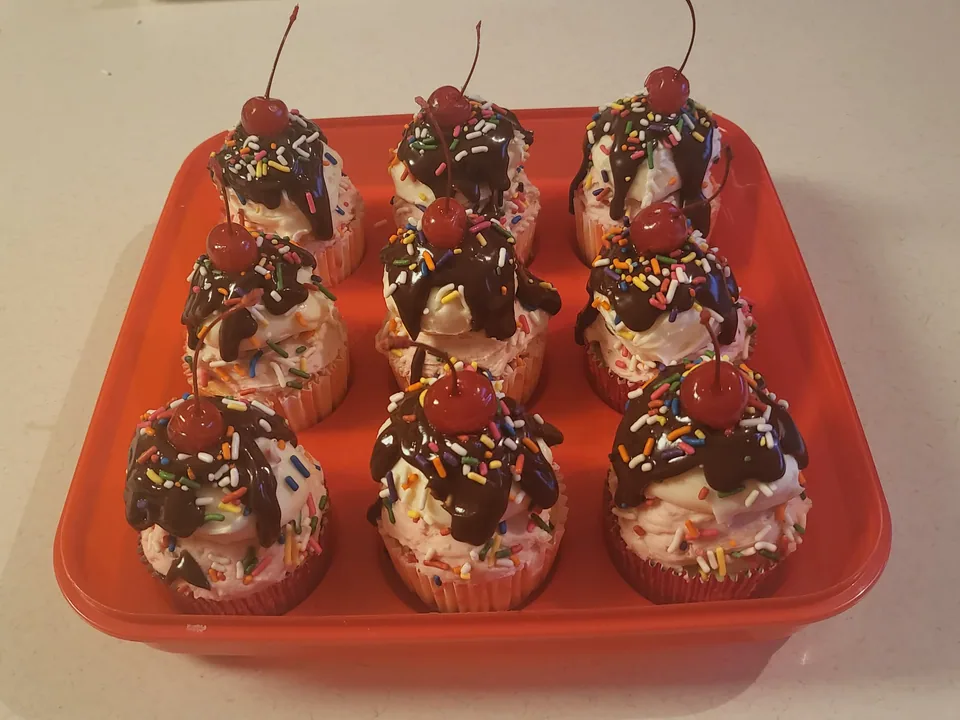 Display of ice cream sundae cupcakes topped with cherries and chocolate drizzle