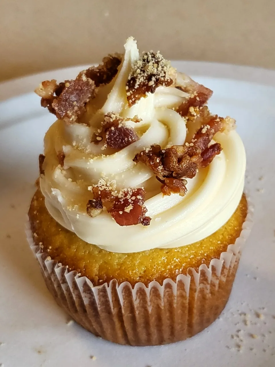 Maple bacon cupcake topped with piped frosting and crisp bacon pieces