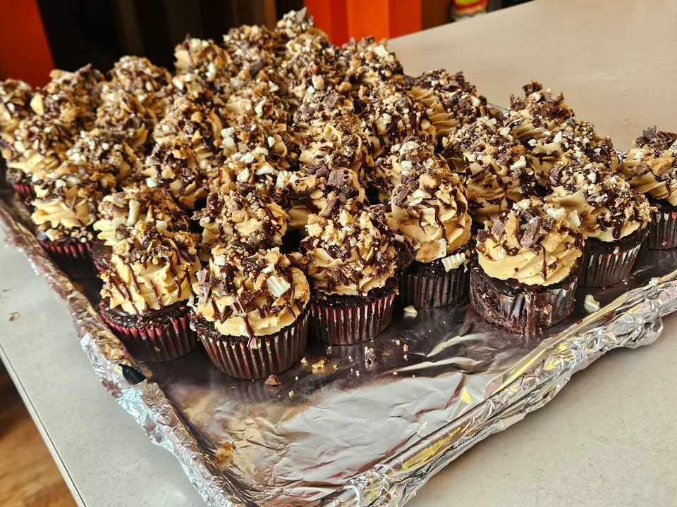 Peanut butter cup cupcakes topped with piped frosting, chocolate drizzle, and chopped candy