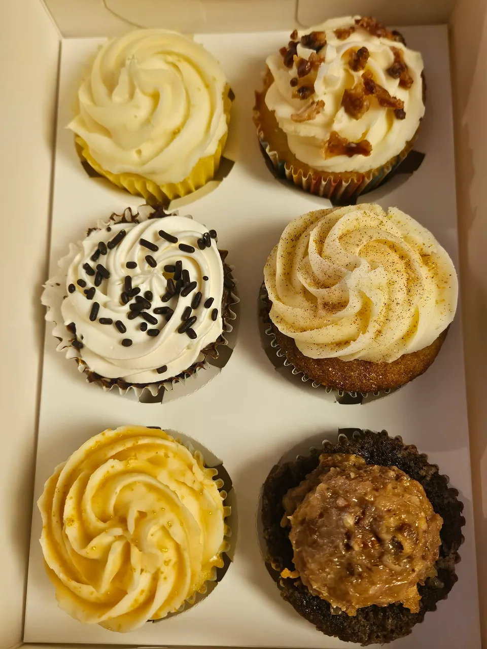 Box of cupcakes with several frosting flavors and finishes