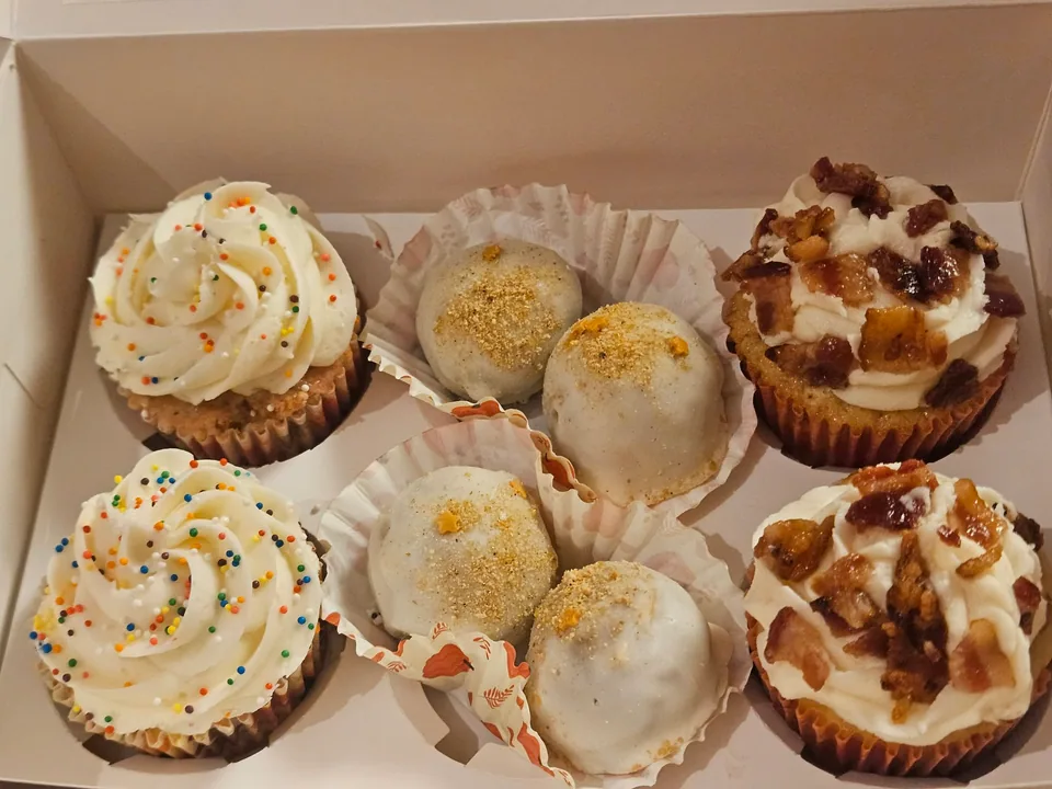 Open bakery box with assorted muffins and decorated cupcakes
