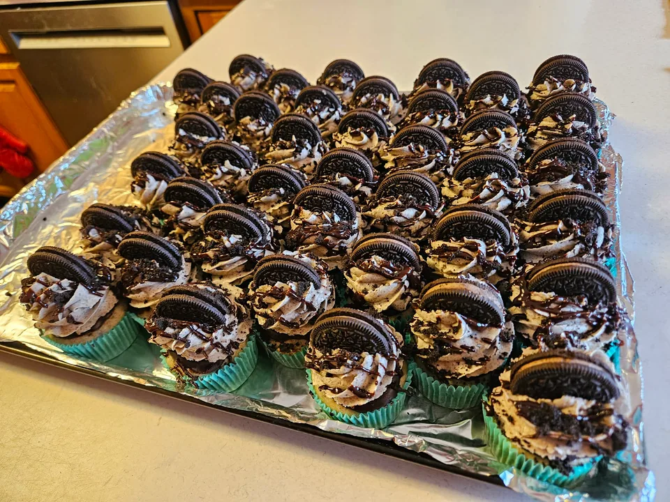 Large tray of Oreo cupcakes topped with cookie pieces and chocolate drizzle