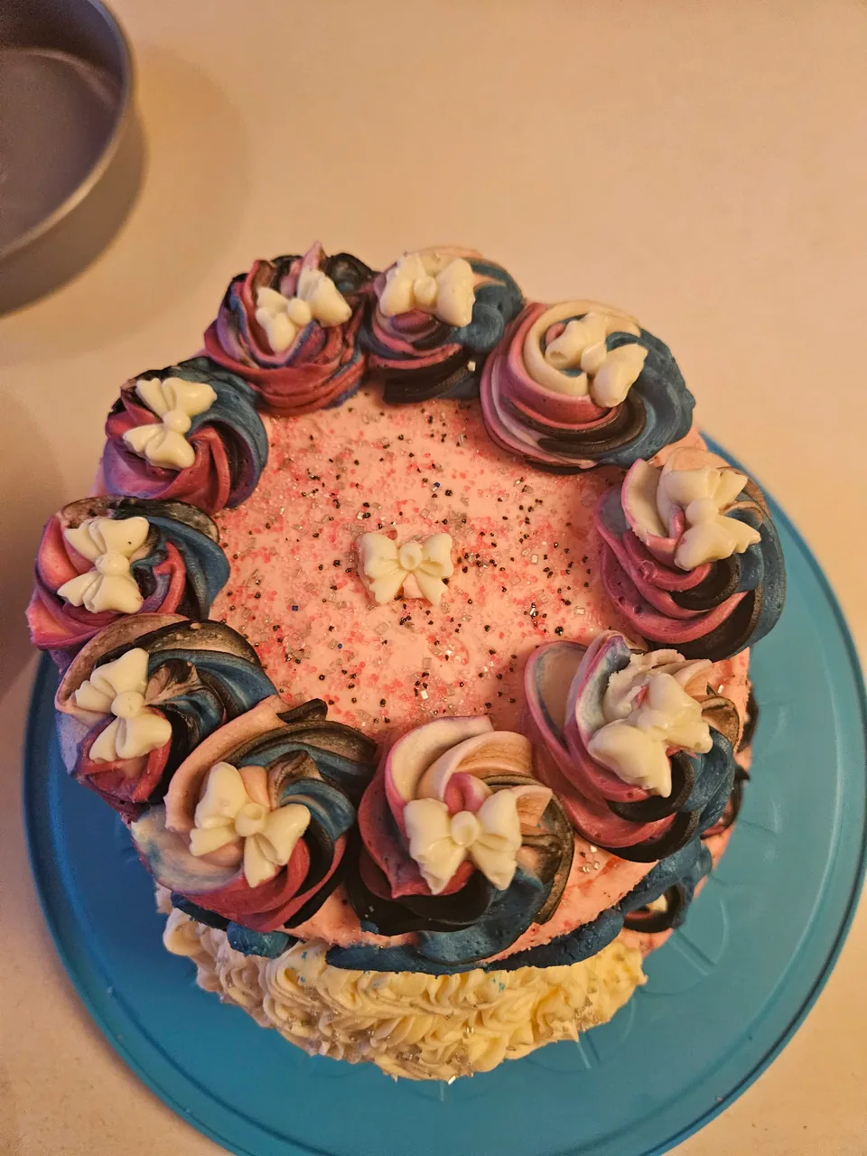 Round cake with pink, blue, and cream piped frosting
