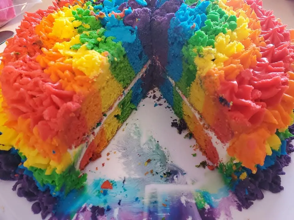 Cut rainbow cake revealing vivid multicolored layers and matching frosting