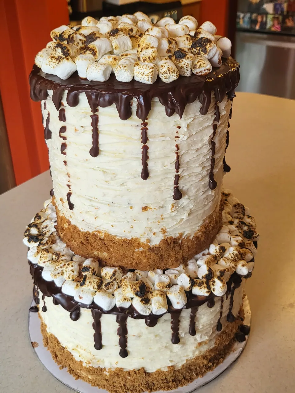 Two-tier s'mores cake with chocolate drip, toasted marshmallows, and graham cracker pieces