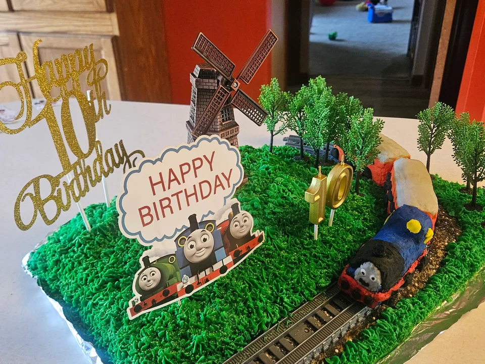 Elaborate birthday cake decorated as a green landscape with a train and windmill