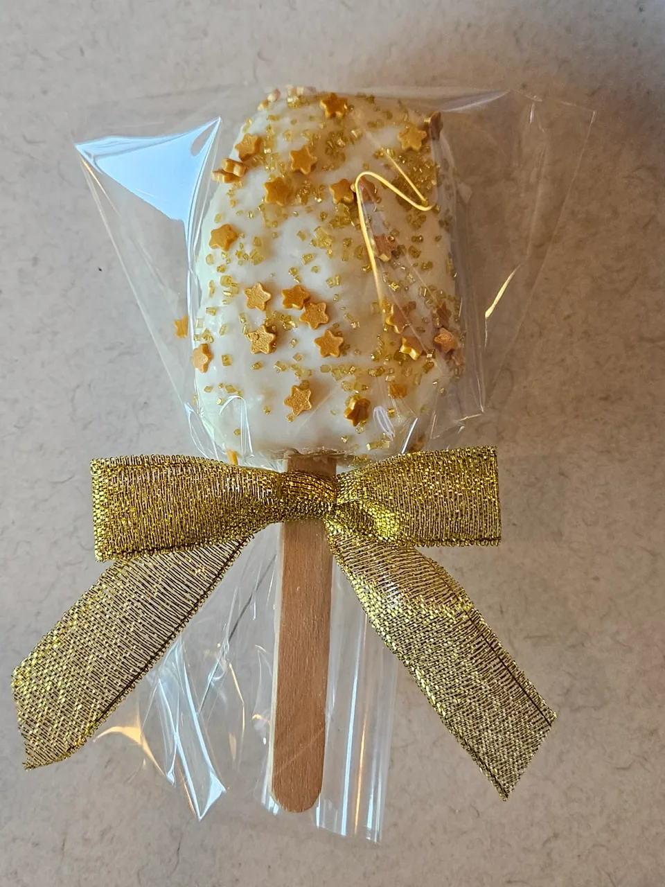 Individually wrapped white chocolate cake pop tied with a gold bow